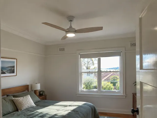 Bedroom with ceiling fan above a bed, window and white walls in Boolaroo